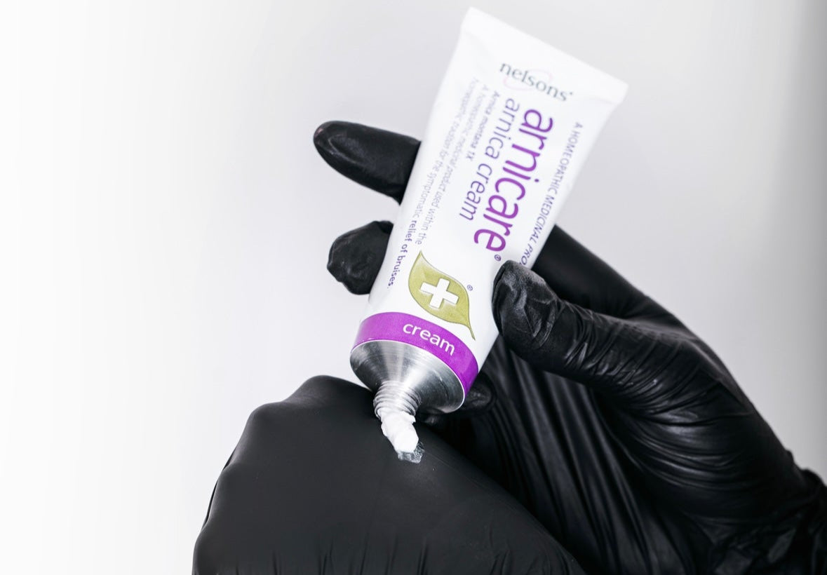 Person wearing black gloves holding a tube of Amicare toothpaste against a white background